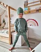 Uśmiechnięty chłopiec w zielonym komplecie dresowym handmade, składającym się z czapki, bluzy oversize i joggerów.