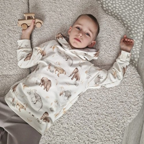 Chłopiec leży na jasnym dywanie w wygodnym komplecie dresowym handmade z motywem zwierząt.
