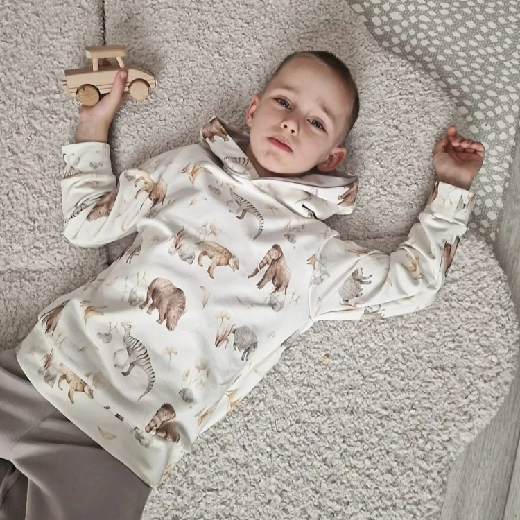 Chłopiec leży na jasnym dywanie w wygodnym komplecie dresowym handmade z motywem zwierząt.