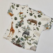 Zbliżenie na t-shirt handmade dla dzieci z motywem safari. Na zdjęciu widać fragmenty wzoru z żyrafą, słoniem, lwem, zebrą i liśćmi monstery.