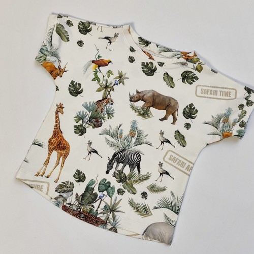 Zbliżenie na t-shirt handmade dla dzieci z motywem safari. Na zdjęciu widać fragmenty wzoru z żyrafą, słoniem, lwem, zebrą i liśćmi monstery.