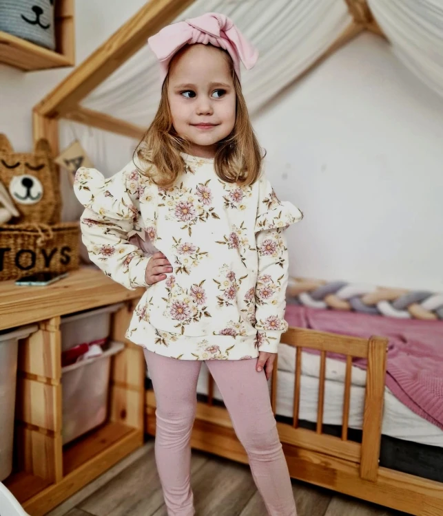 Dziewczynka w komplecie handmade: bluza w stokrotki i różowe legginsy.